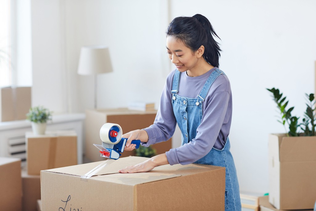 end of tenancy moving out, asian woman packing boxes and sealing them with tape