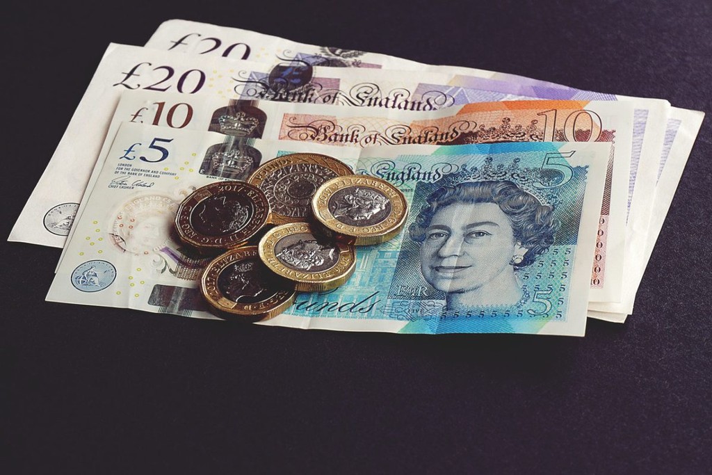 A small pile of English bank notes with 5 coins on top.