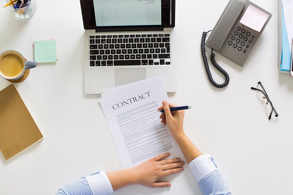 signing a contract next to a laptop, mug and phone