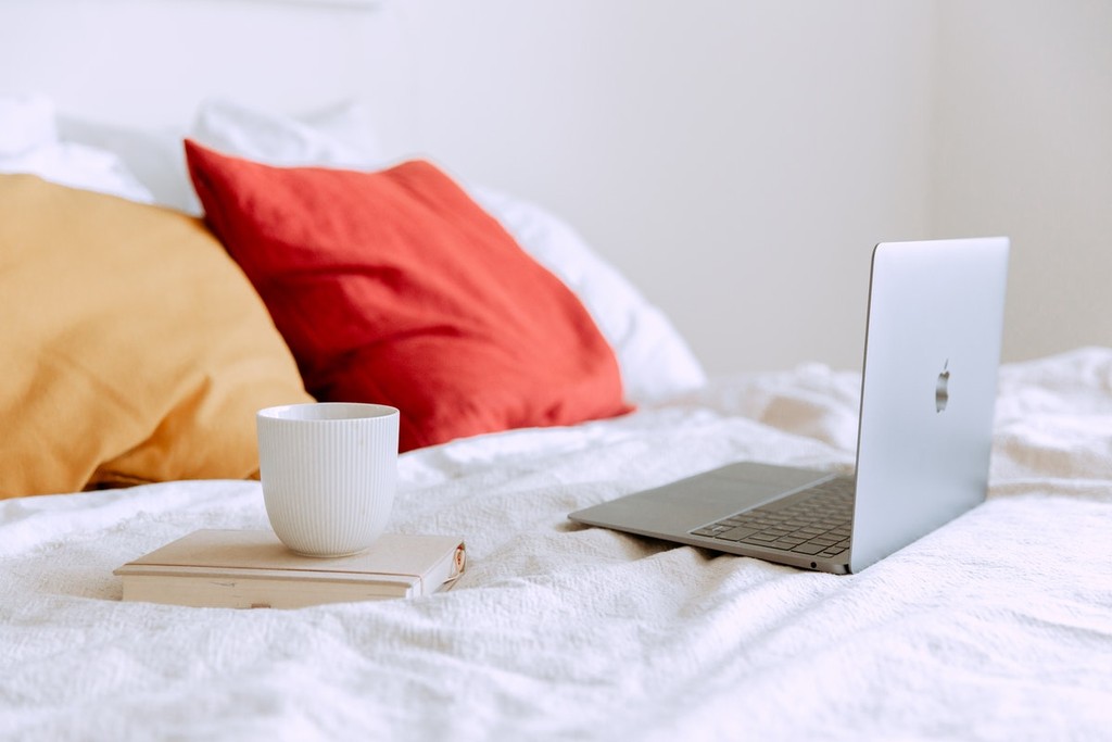 apple macbook air on a stylish bed next to a book and cup