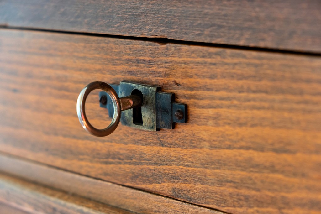 Secret, mystery privacy concept. Retro key on an old fashioned keyhole, wooden drawer background close up view. Vintage furniture detail