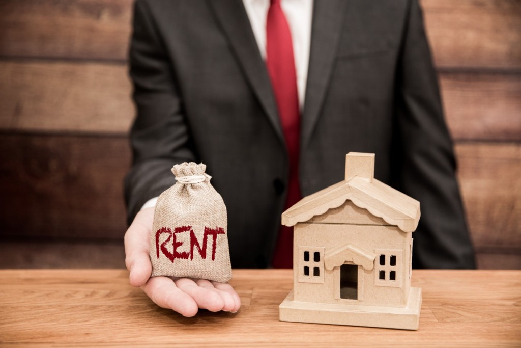 landlord holding a rent package next to a wooden house