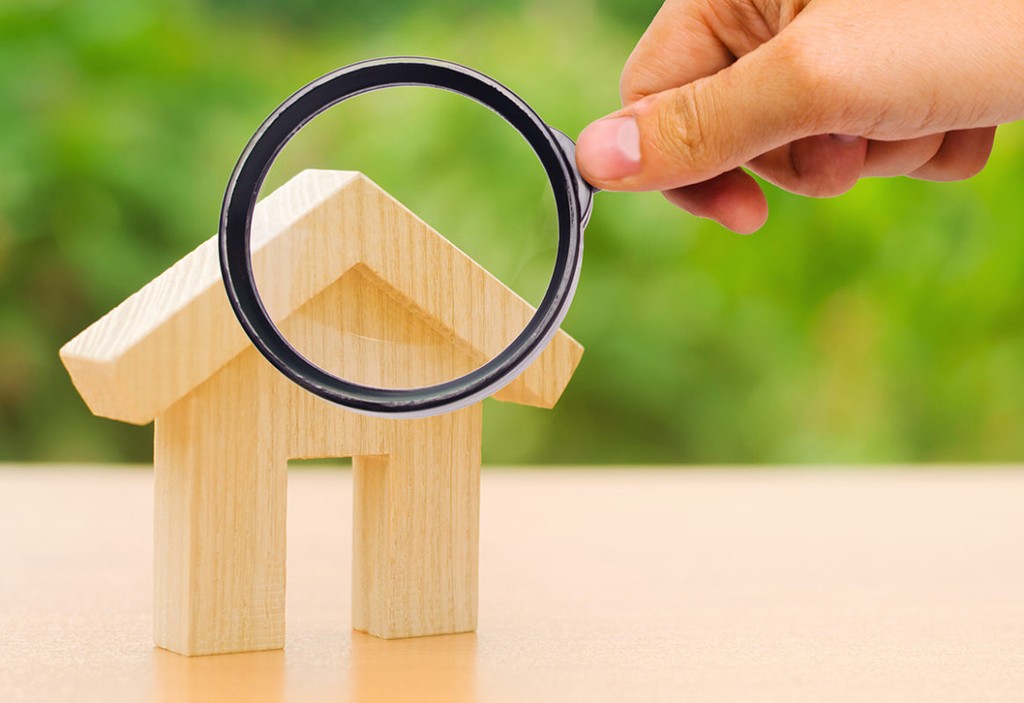 A magnifying glass looks at a wooden house. The concept of buying and selling real estate, renting. Search for a house. Affordable housing, credit and loans. Investments