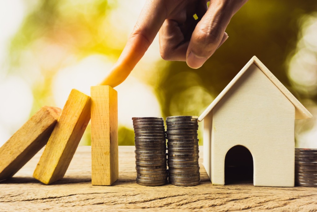 Home or real estate insurance protection concept. A man hand stop a wooden dominoes continuous toppled before reaching the house and money. Depicts preventing losses that will occur to the property.