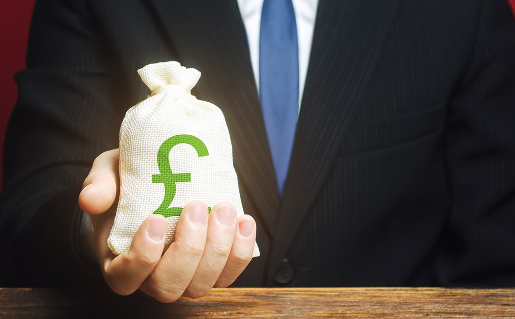 Man holds out a Pound sterling GBP money bag. Provision of money on credit, grant. Project financing. Donations. Financial social assistance. Payment purchases, profits dividends. Business investment