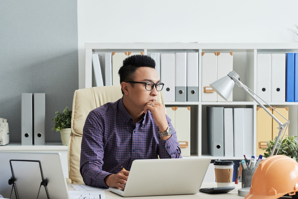 asian man with thinking expression at a desk with laptop