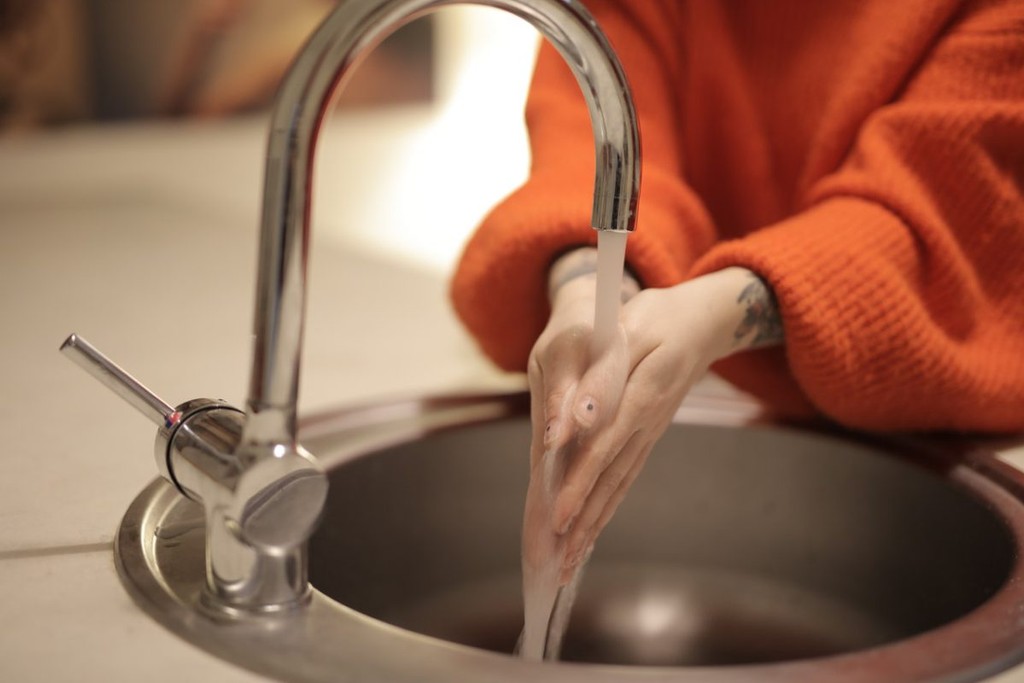 landlord in an orange jumper washing their hands at a kitchen sink