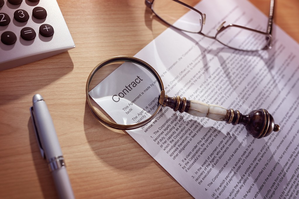 Magnifying glass examining and signing a legal contract document with a break clause