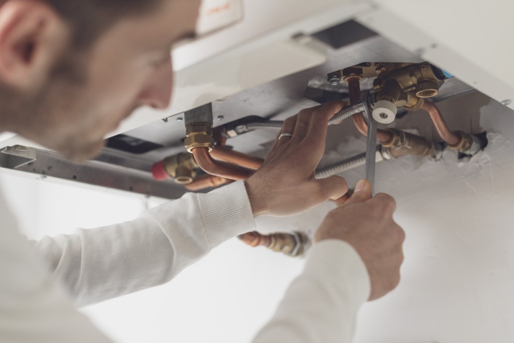 Professional plumber checking a boiler and pipes, he is using a wrench