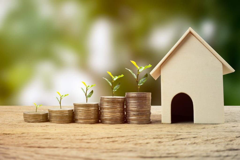 Real estate investment, Money savings for buy new home, Financial wealth management concept. A plant growing on stacked coins with wooden house model. Depicts the growth of the real estate business.