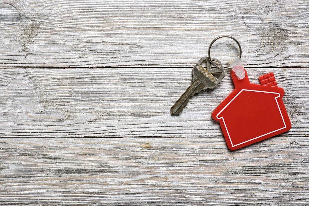 House key on a red color house shaped keychain resting on wooden floorboards concept for buy-to-let mortgages, moving home or renting property