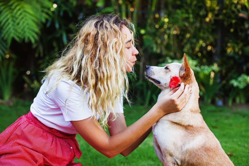 woman kissing a dog and placing a flower by his ear