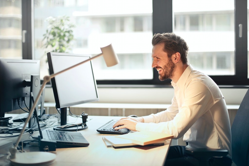 man smiling at laptop looking for proptech companies