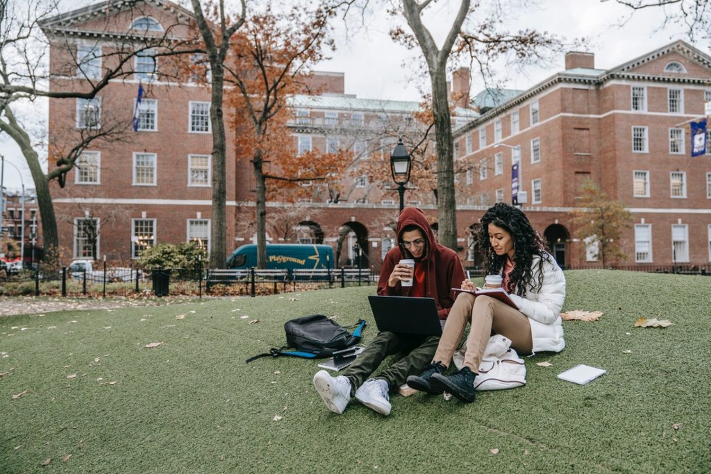 students sitting outside a campus building on the grass