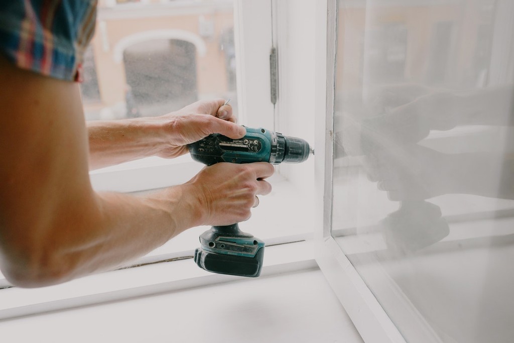 man drilling hinges on a window