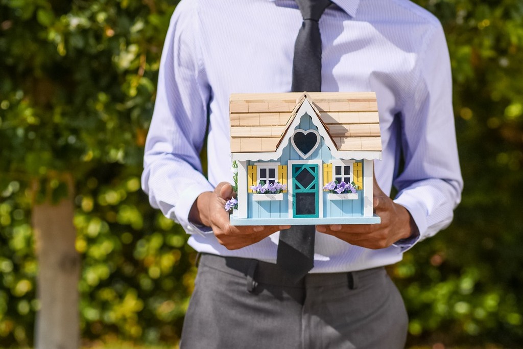 man in purple shirt holding wooden house