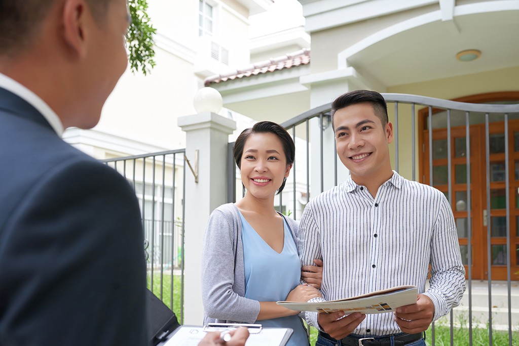 Cheerful young Vietnamese family talking to real estate agent conducting house viewing in front of house