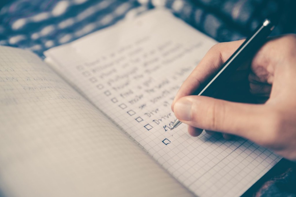 Person planning out tasks, using check boxes, on a A5 notepad. They are using black pen