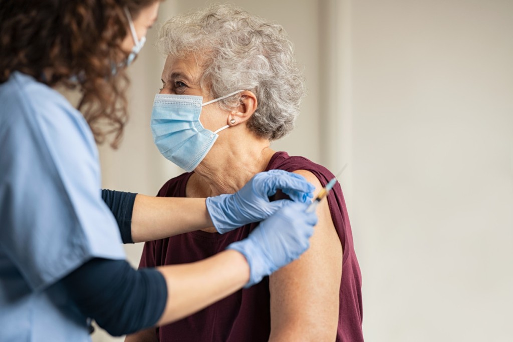 General practitioner vaccinating old patient in private clinic with copy space. Doctor giving injection to senior woman at hospital. Nurse holding syringe and using cotton before make Covid-19 or coronavirus vaccine