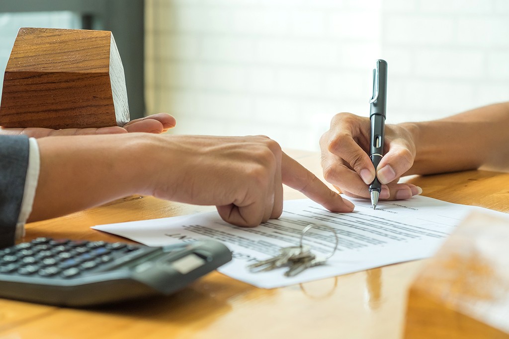 contract being signed between two parties on a wooden table next to keys and a calculator