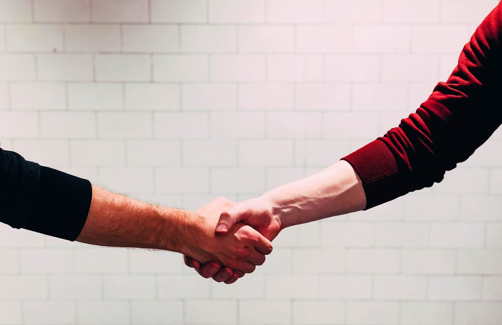 two people shaking hands against a white brick wall