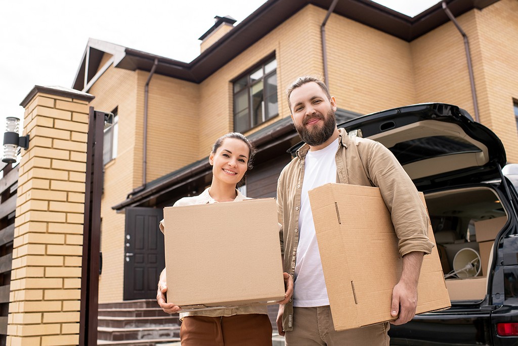 man and woman holding boxes outside a new home