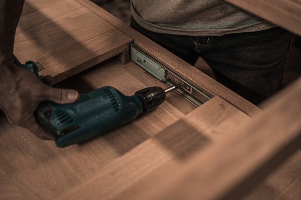 A property manager is using a drill to fix flooring