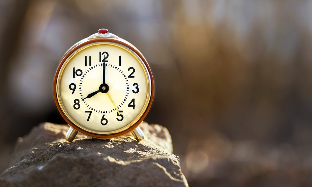 Time concept - red alarm clock standing on a stone