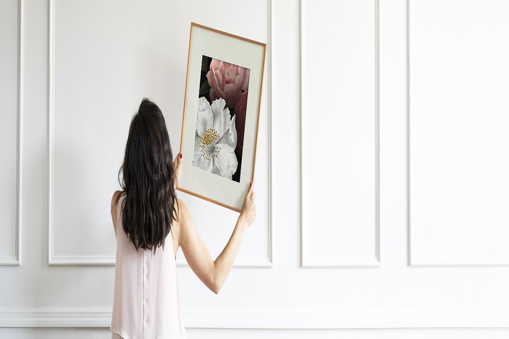 lady hanging art on a white wall in her home