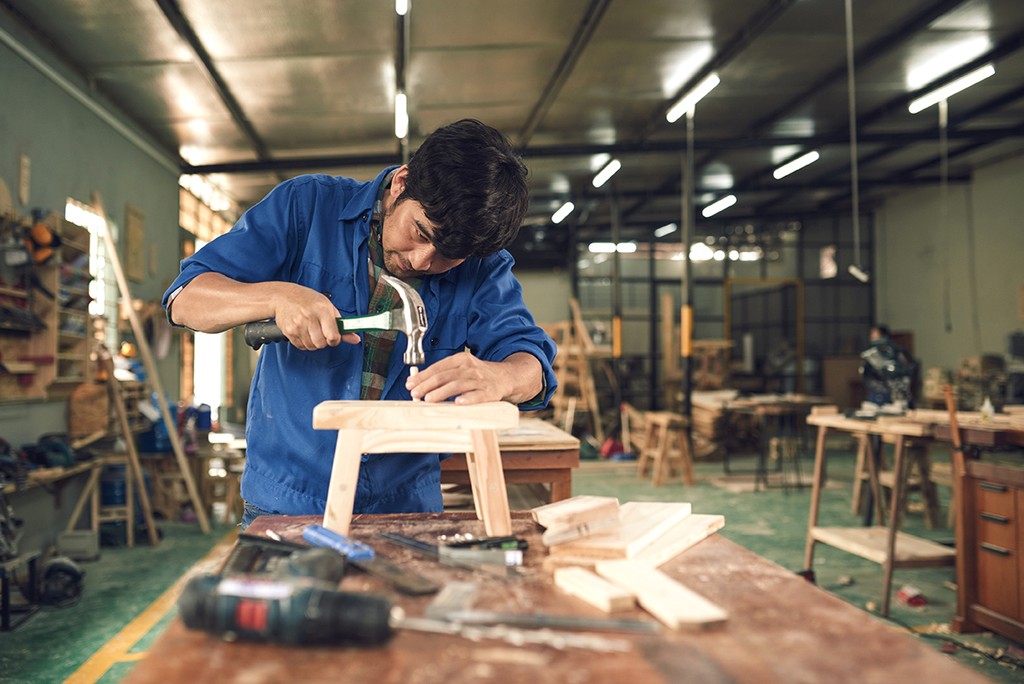 Carpenter hammering nail into wooden chair in workshop