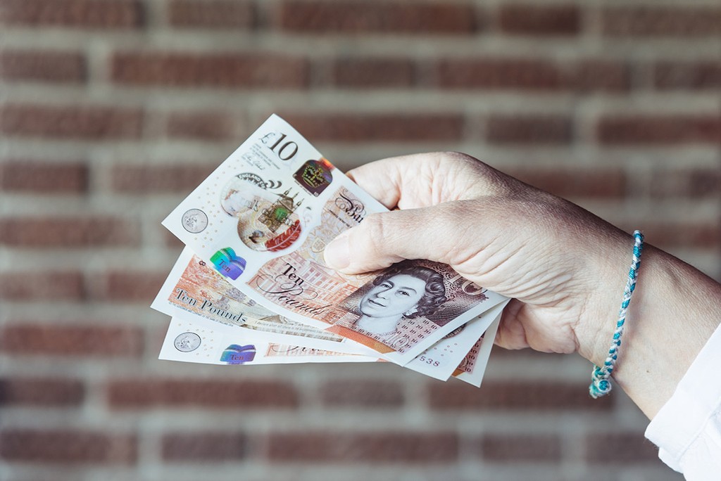 Close up of hand of woman holding pounds sterlings against brick wall background