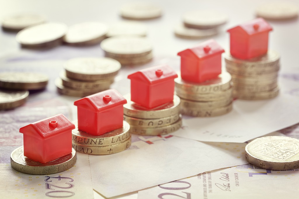 Minature houses resting on pound coin stacks concept for property ladder, mortgage and real estate investment