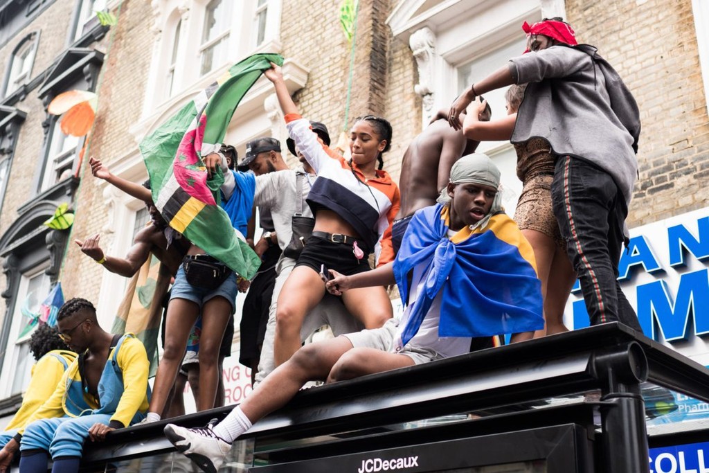 People with flags sitting on a bus stop during Notting Hill Carnival