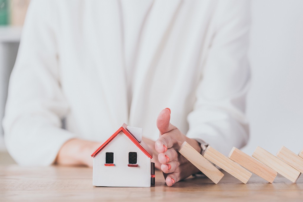 partial view of risk manager protecting house model from falling wooden blocks with hand. buy-to-let mortgage risks concept