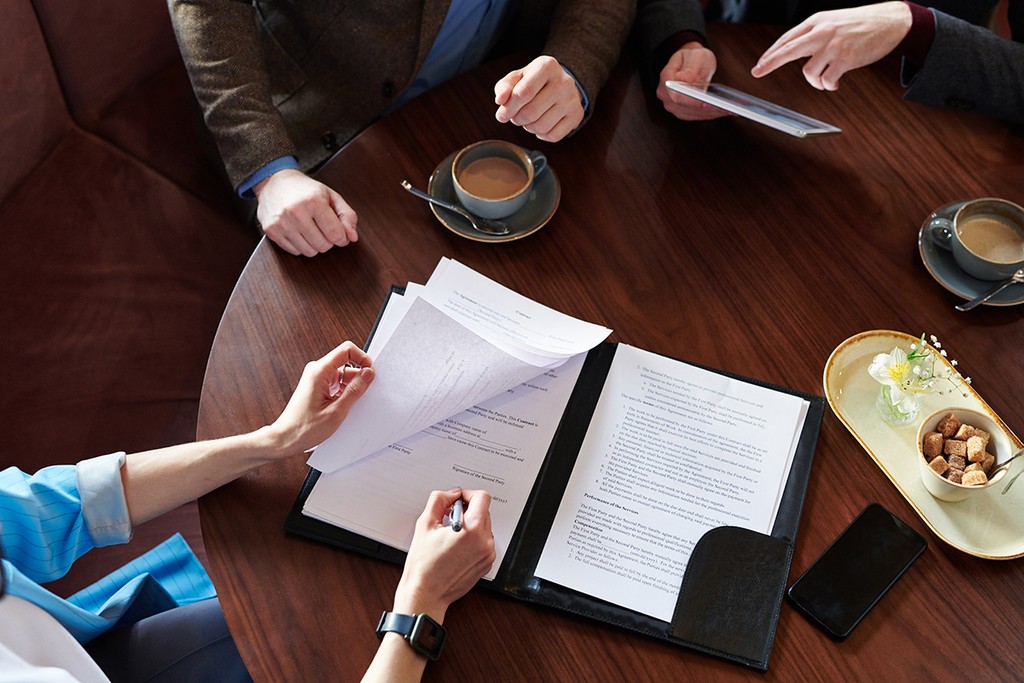 Above view of unrecognizable businesswoman signing contract after negotiation with business partners in cafe